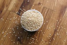 sesame seeds in a small white bowl on a wooden table with other grains scattered around