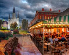 an outdoor cafe with people sitting at tables in front of it and the sky is dark