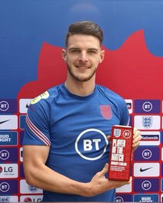 a man holding a plaque in front of a red and blue wall with england crests on it