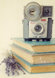 an old camera is sitting on top of two books and lavenders are next to it