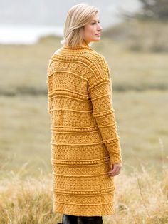 a woman standing in tall grass wearing a mustard colored cardigan and black leather boots