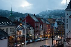 a city street filled with lots of traffic next to tall buildings in the snow covered mountains