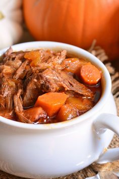 a white bowl filled with meat and carrots on top of a woven table cloth