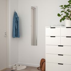 a room with white furniture and a plant on top of the dresser next to it