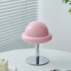 a pink lamp sitting on top of a white table next to a potted plant