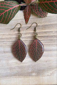 red and green leaf earrings sitting on top of a wooden table next to a potted plant