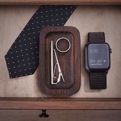 an apple watch, tie and other items are on display in a wooden case with a black dotted necktie