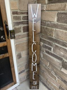 a wooden welcome sign sitting next to a brick wall in front of a door with the word welcome written on it