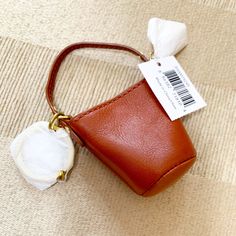 a small brown purse with a white flower on the side and a price tag attached to it