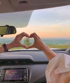 two people making a heart shape with their hands in the back seat of a car