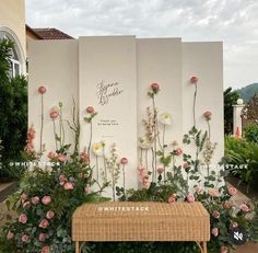 a wooden bench sitting in front of a white wall with flowers on it's side