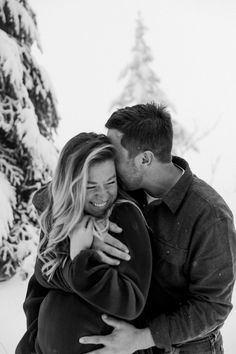 a man and woman hugging in the snow with trees in the backgrouds