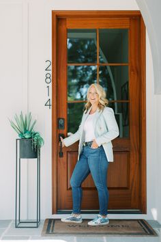 a woman standing in front of a door with her hands in her pockets and smiling