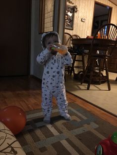 a toddler standing in the middle of a living room drinking from a sippy cup