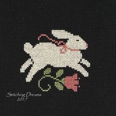 the cross stitch pattern shows a white sheep with a pink rose in its mouth, on a black background