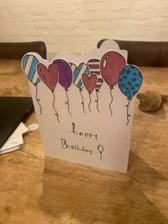 a happy birthday card with balloons on it sitting on a table next to a laptop