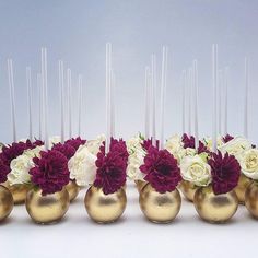 a row of gold vases filled with white and red flowers on top of each other