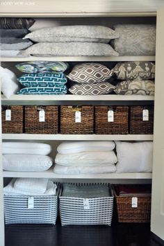 an organized closet with white linens, pillows and baskets on the bottom shelf for storage