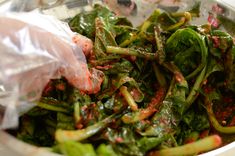 a white bowl filled with green vegetables covered in plastic wrapper next to a spoon