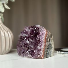 a purple rock sitting on top of a white table next to a vase filled with flowers