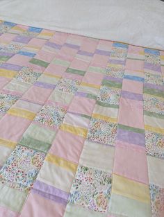 an unmade bed with pink, yellow and green quilted bedspread on it