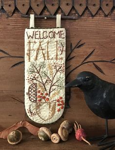 a black bird sitting on top of a wooden table next to a sign that says welcome fall