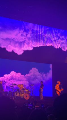 two men are on stage playing instruments in front of an audience with purple lighting behind them