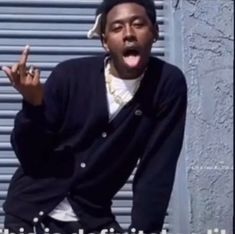 a man with his tongue out standing in front of a garage door and making the peace sign