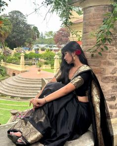 a woman in a black and gold sari sitting on a stone wall with stairs behind her