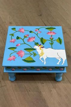 a painted wooden box with a cow on it's side and flowers in the background