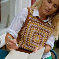 a woman sitting at a table writing on a piece of paper with a pen in her hand