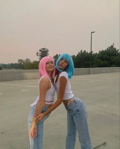 two women with pink and blue hair are hugging each other in an empty parking lot