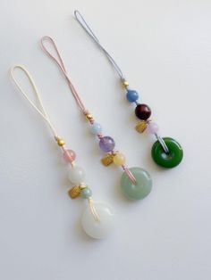 three necklaces with different colored beads hanging from each other on a white table top