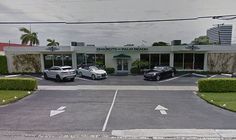 two sports cars parked in front of a dealership with palm trees on the other side