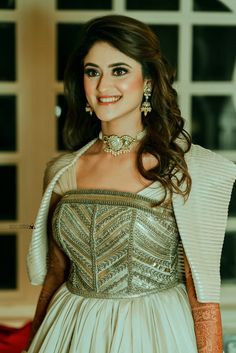 a woman in a white dress and gold jewelry smiling at the camera with her hand on her hip