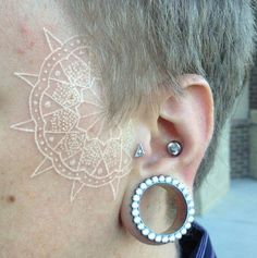 a woman with white paint on her face and behind her ear is an intricate design