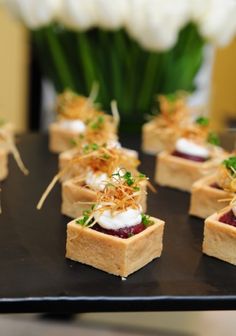 small appetizers are arranged on a black tray with white flowers in the background