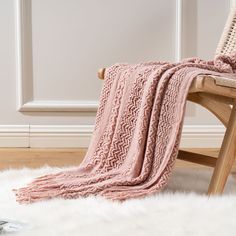 a pink blanket sitting on top of a wooden chair next to a white sheepskin rug