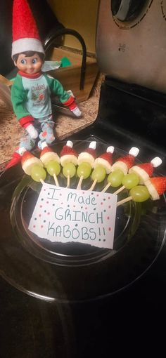 an elf is sitting on top of a plate with fruit skewers in front of him