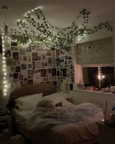 an unmade bed with lots of pictures on the wall and lights hanging from the ceiling