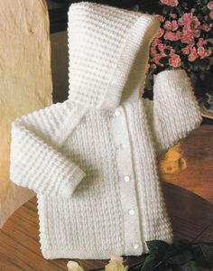 a white knitted sweater sitting on top of a wooden table next to some flowers