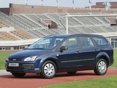 a small blue car parked in front of an empty stadium bleachers and grass