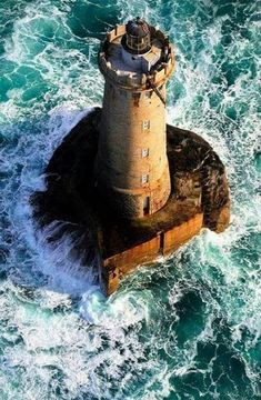 an aerial view of a lighthouse in the middle of the ocean with waves crashing around it