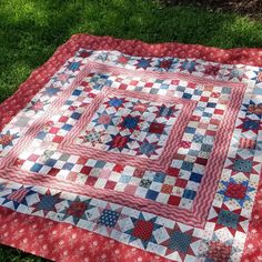 a red and white quilt on the ground with grass in the backgroung