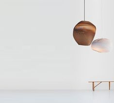 two lamps hanging from the ceiling next to a table and bench in front of a white wall