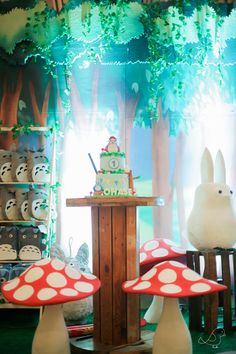 a table topped with lots of cakes and mushrooms in front of a forest scene filled with fake trees