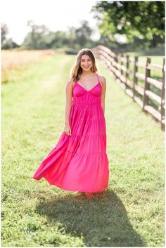 a beautiful young woman in a pink dress standing by a fence smiling at the camera