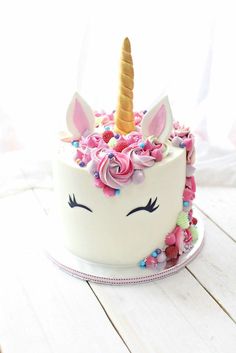 a white cake with pink frosting and a unicorn's face on top, surrounded by sprinkles