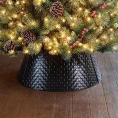 a christmas tree with pine cones and lights in a black pot on a wooden floor