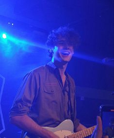 a man playing guitar in front of a microphone and some people on stage with lights behind him